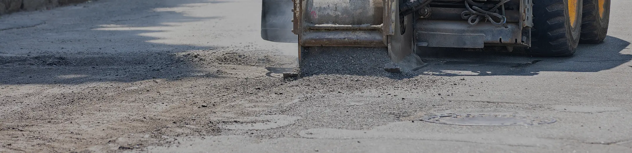 Close-up of an asphalt milling machine removing the top layer of pavement to prepare the surface for repaving