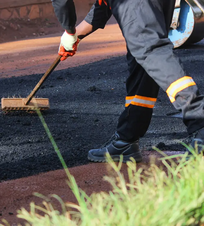 Worker applying fresh asphalt with a rake during paving installation in Phoenix, AZ