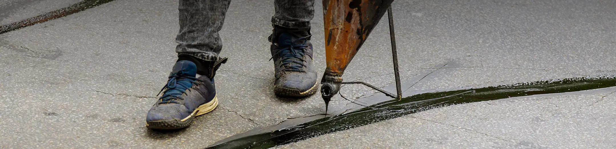Close-up of a worker sealing cracks in asphalt with liquid sealant