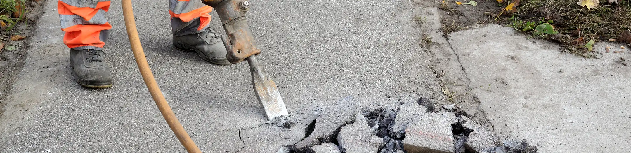 Construction worker using a jackhammer to break cracked asphalt pavement in Phoenix, Arizona