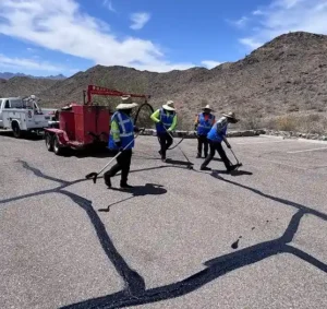 Crack sealing process on asphalt parking lot with workers and sealant equipment