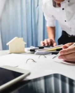 Businessperson working at a desk with tablet, documents, and house model