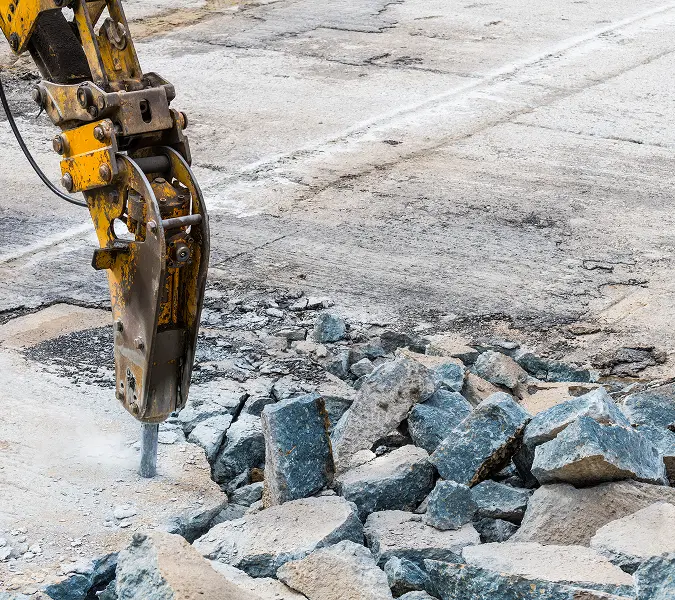 Excavator hydraulic breaker demolishing asphalt pavement into rubble for site clearing in Phoenix, Arizona