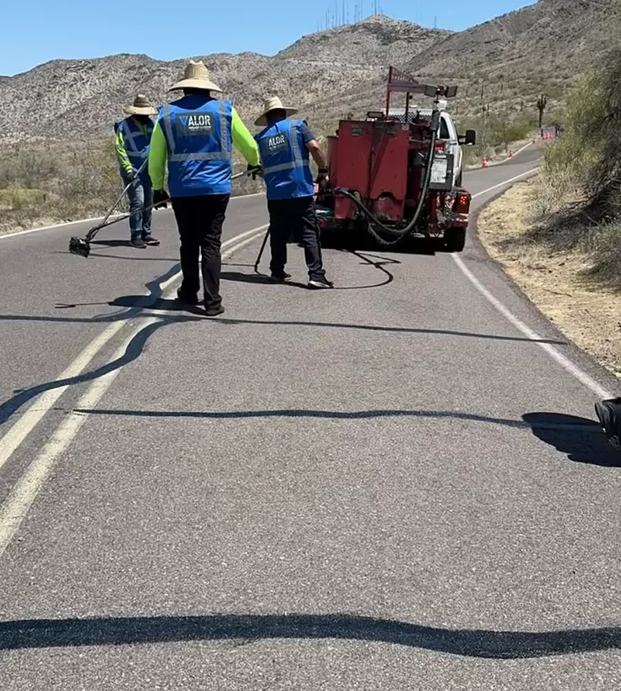 Crew applying crack sealant on a rural asphalt road using specialized equipment