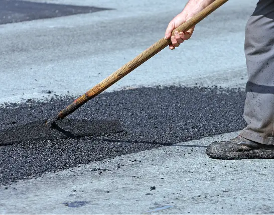 Worker using a tool to spread fresh asphalt over a road surface for patching