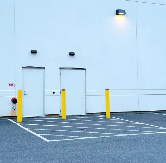 Exterior of a commercial building with fresh pavement markings and safety bollards near service doors