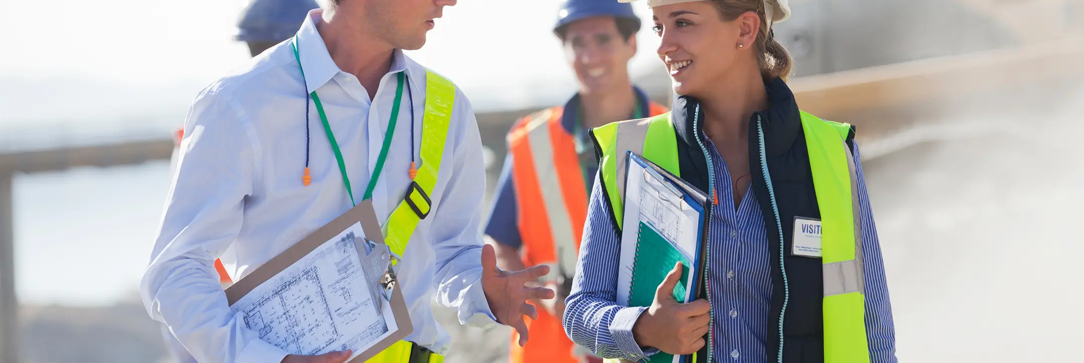 Construction professionals wearing safety vests and helmets engaged in conversation at a worksite