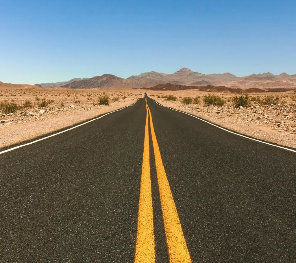 Straight paved road in the Arizona desert leading toward mountains under a clear blue sky