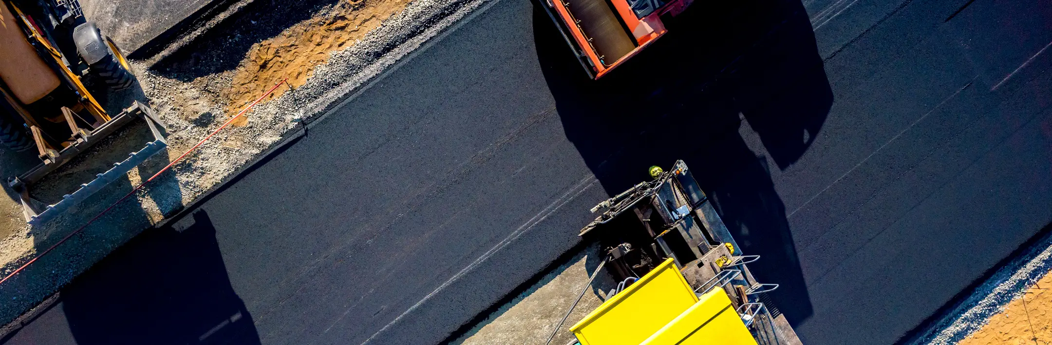Aerial view of heavy machinery laying fresh asphalt on a road construction site