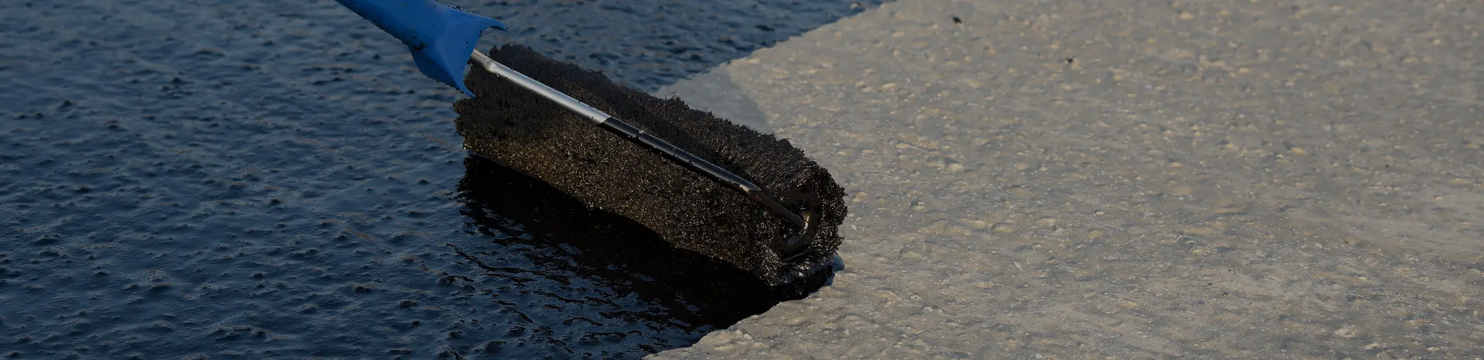 Close-up of a roller applying seal coat to asphalt pavement