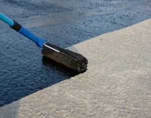 Worker applying sealcoat to asphalt surface with a roller brush