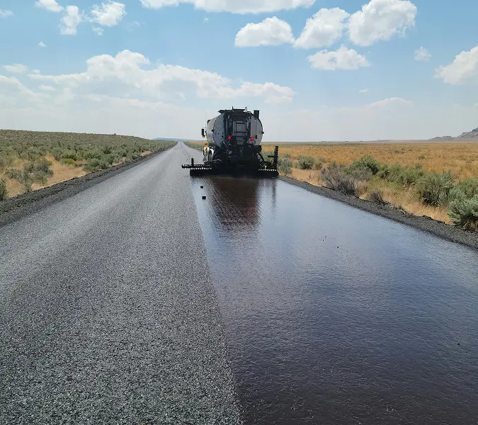 Sealcoating truck applying protective layer on a rural asphalt road