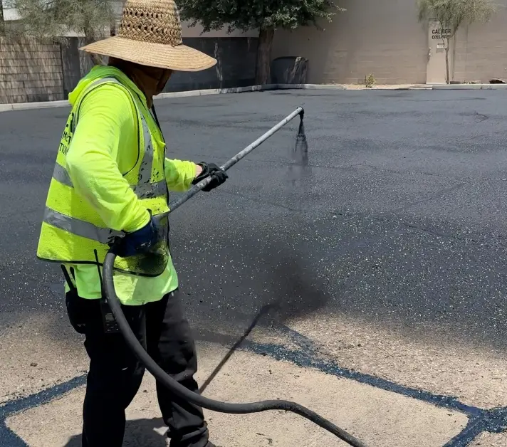 Worker applying asphalt sealcoating during parking lot maintenance in Mesa, AZ