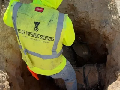 Worker repairing a broken drain pipe during a parking lot maintenance project at Imagine Rosefield Charter School in Phoenix, AZ.