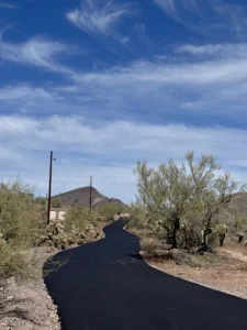Completed private road curving through Desert Hills with fresh asphalt, saguaro cacti, and a desert mountain in the background