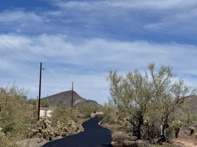 Completed private road curving through Desert Hills with fresh asphalt, saguaro cacti, and a desert mountain in the background
