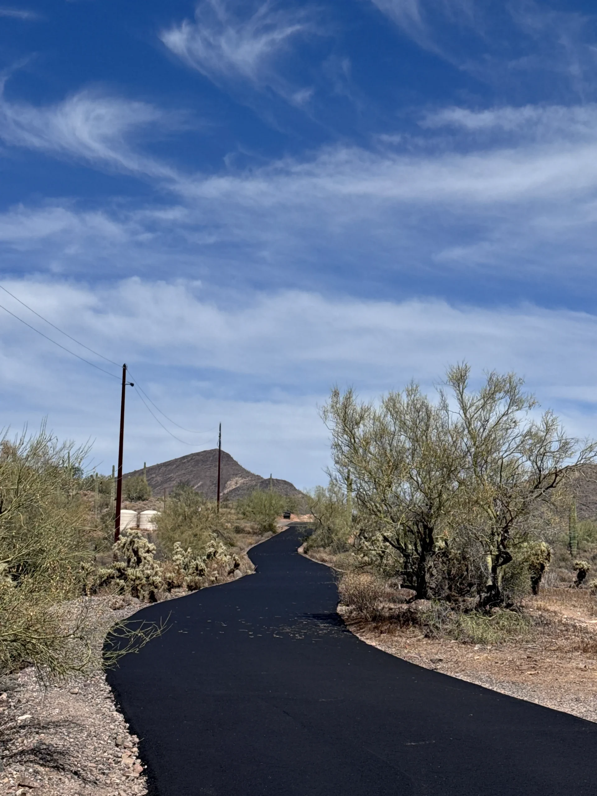 Completed private road curving through Desert Hills with fresh asphalt, saguaro cacti, and a desert mountain in the background