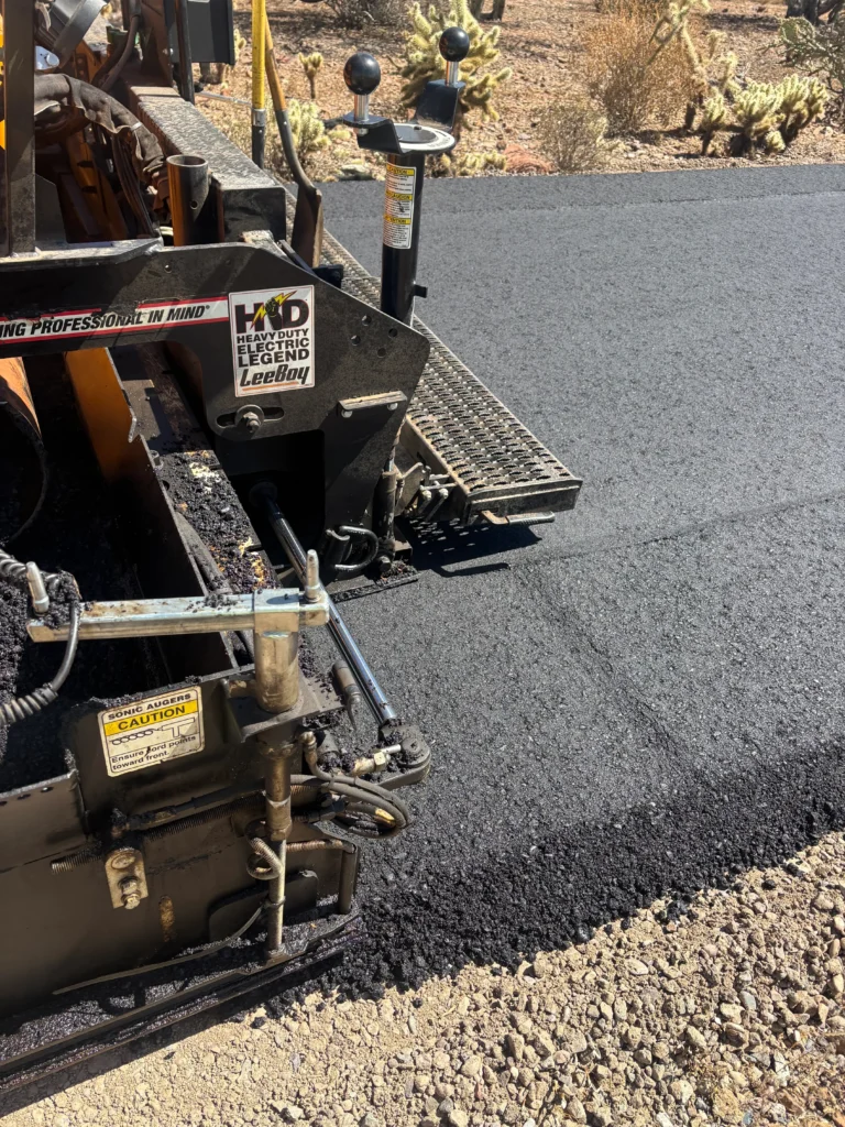 Paver laying fresh hot mix asphalt on prepared aggregate base course during Desert Hills road construction