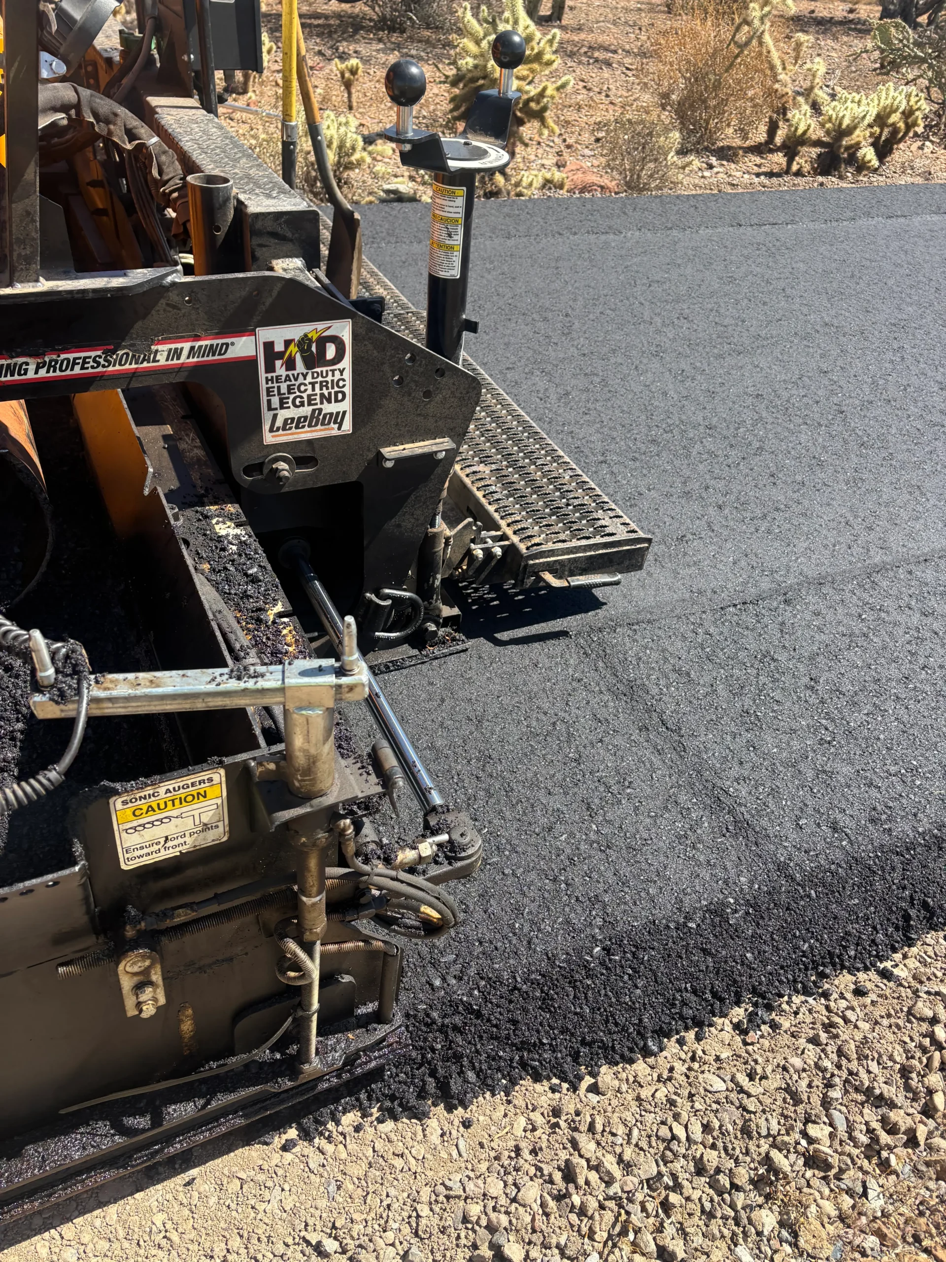 Paver laying fresh hot mix asphalt on prepared aggregate base course during Desert Hills road construction